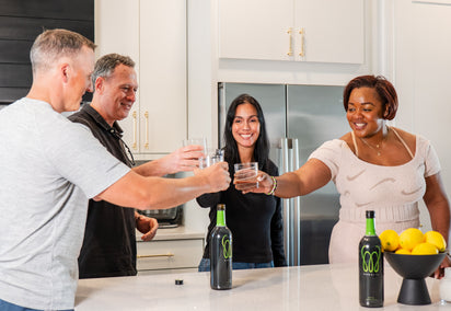 A diverse group of friends smiling and clinking glasses in a kitchen for a Monavie Active toast.