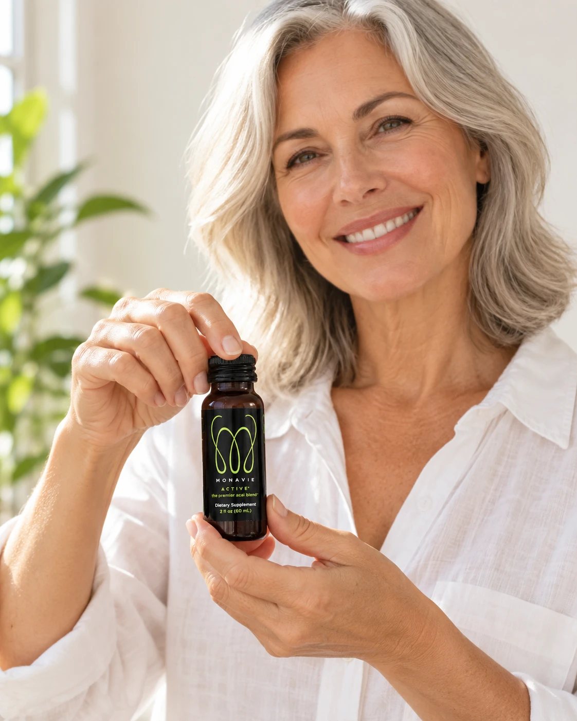 Smiling woman with silver hair holding up a MonaVie Active 2 oz shot
