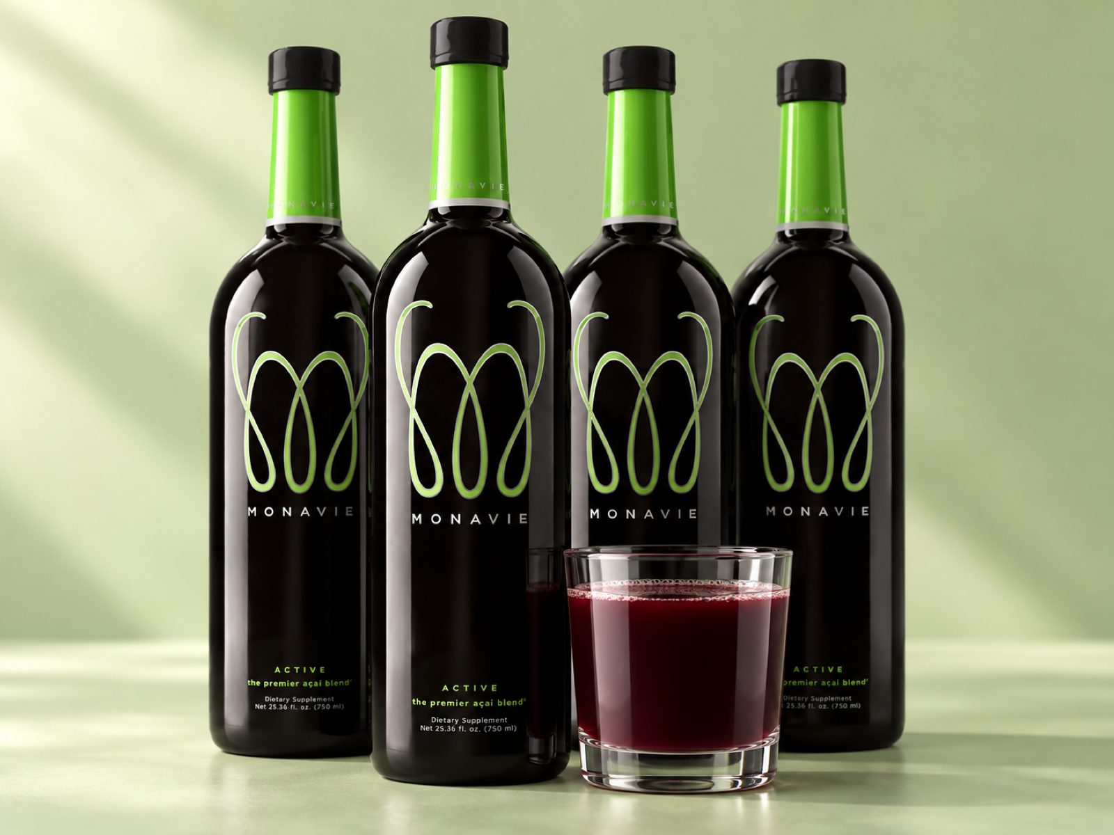 Four MonaVie Active 25 oz bottles standing behind a glass filled with the dark juice