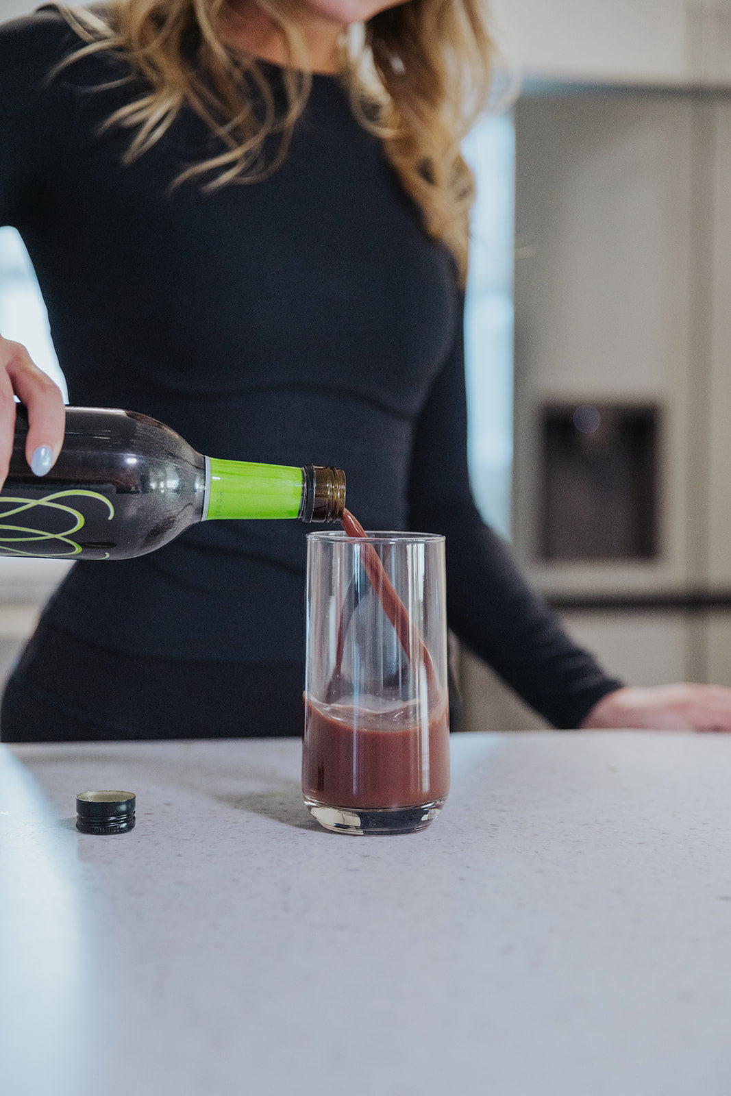 Woman pouring MonaVie Active into a tall glass on a kitchen counter