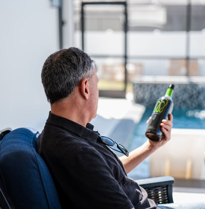 A man sitting in a patio chair by a pool, holding a bottle of Monavie Active and looking out at the water.