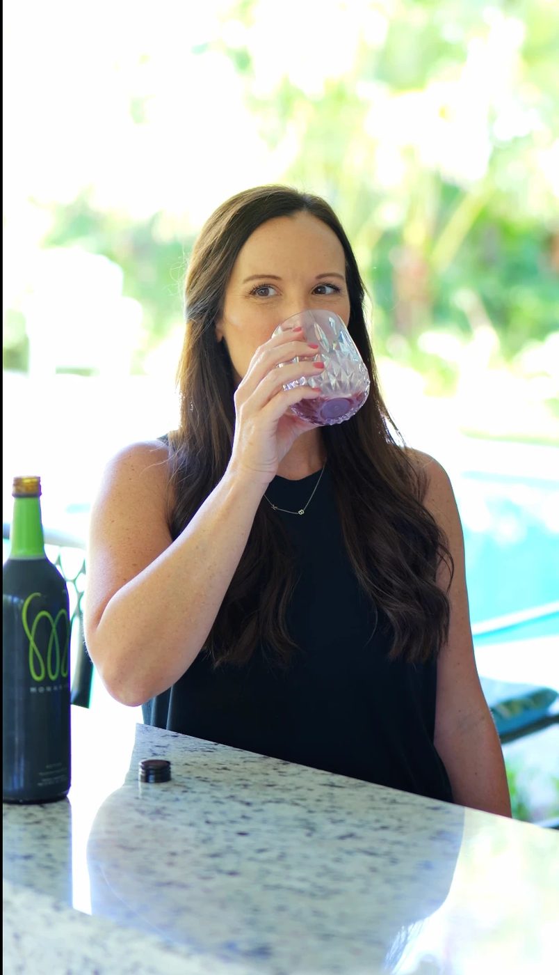 Woman enjoying a glass of MonaVie Active at an outdoor bar with the bottle beside her